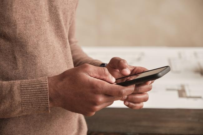 Una fotografía muestra las manos de un hombre usando su teléfono celular inteligente