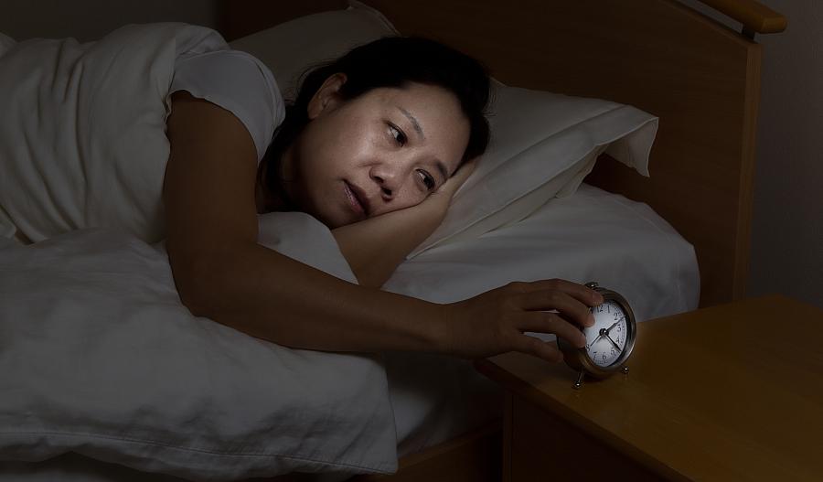 Imagen de una mujer despierta en la cama tocando el despertador