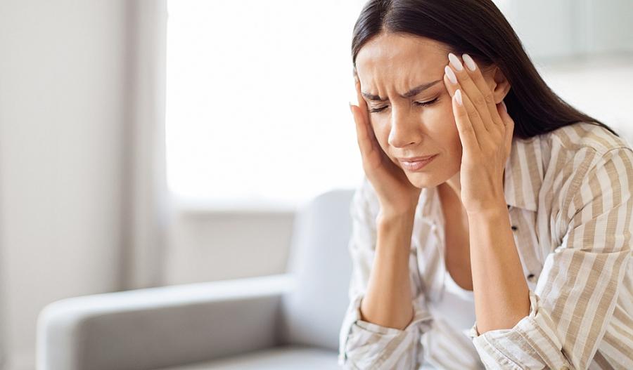 Una fotografía muestra a una mujer con sus ojos cerrados, con sus manos en los costados de su cabeza, en actitud de dolor.